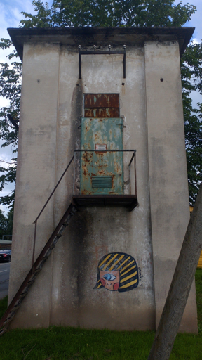 electro tower with rusty door and graffiti of a one-eyed girl's head with black/yellow striped hair