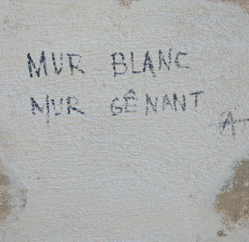 the words "mur blanc mur gênant" with a small anarchy A scribbled with black pen on rough white wall
