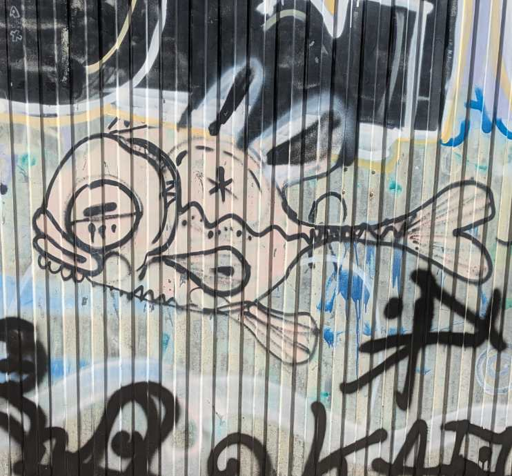 fish doodled with spray paint. light grey fillcolor and black lines. sprayed on grey uneven surface with other graffiti nearby