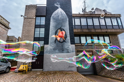 A large mural of a goldfish inside a plastic bag of water, with the anarchist A drawn on the inside of the bag as if by the fish