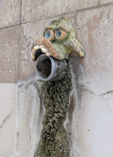 ceramic that looks like the face of a goblin or another fantasy creature. the face is placed above a water pipe which makes the pipe look its part of the mouth